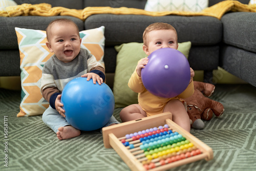 Two toddlers playing with balls and abacus sitting on floor at home