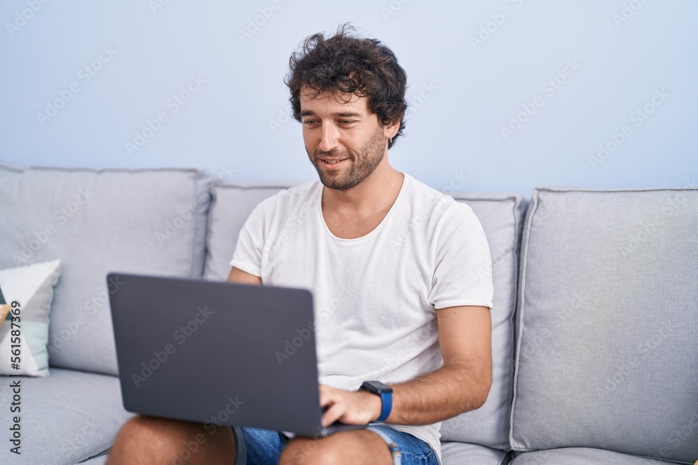 Young hispanic man using laptop sitting on sofa at home