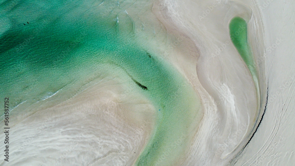 Beach with wavy blue water coming into it, as seen from a drone
