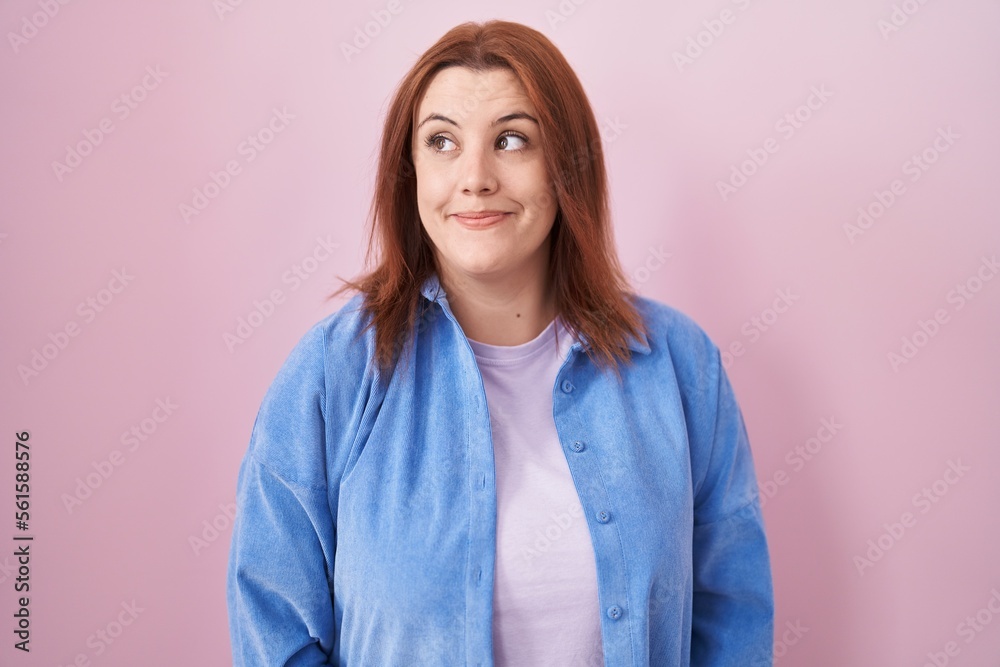 Young hispanic woman with red hair standing over pink background smiling looking to the side and staring away thinking. Young hispanic woman with red hair standing over pink background smiling looking to the side and staring away thinking.