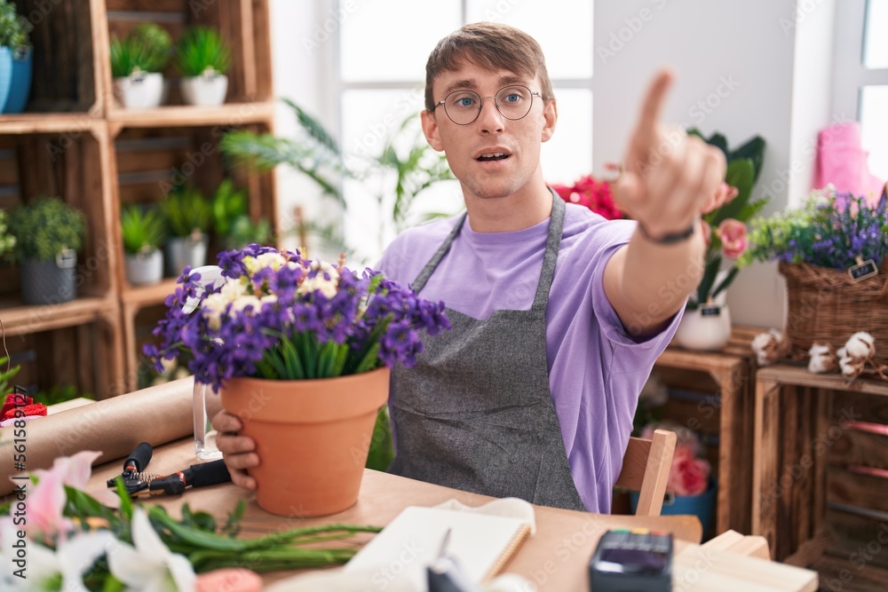 Caucasian blond man working at florist shop pointing with finger surprised ahead, open mouth amazed expression, something on the front