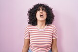 Young middle east woman standing over pink background angry and mad screaming frustrated and furious, shouting with anger. rage and aggressive concept.
