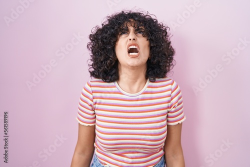Young middle east woman standing over pink background angry and mad screaming frustrated and furious, shouting with anger. rage and aggressive concept.