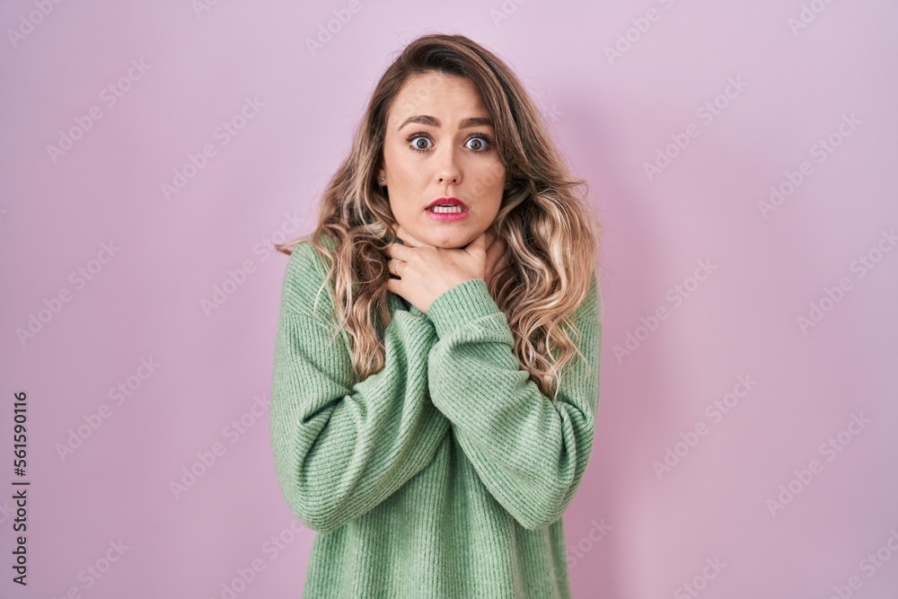 Fototapeta premium Young caucasian woman standing over pink background shouting and suffocate because painful strangle. health problem. asphyxiate and suicide concept.