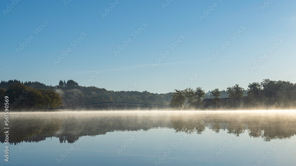 Fototapeta premium Passerelle du Lac de Saint Pardoux at sunrise in autumn with fog on the water