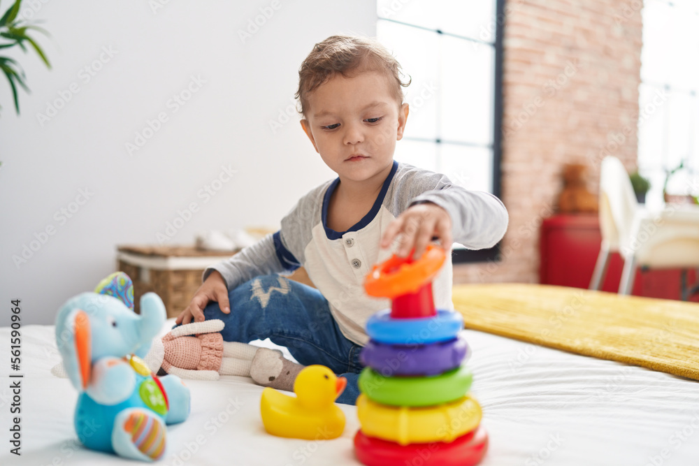Adorable caucasian boy playing with hoops toy sitting on bed at bedroom Adorable caucasian boy playing with hoops toy sitting on bed at bedroom
