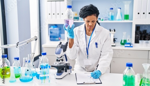 African american woman wearing scientist uniform measuring liquid at laboratory