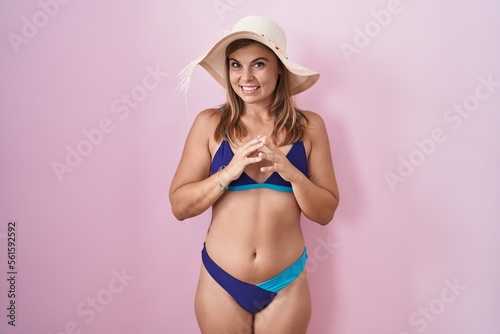 Young hispanic woman wearing bikini over pink background hands together and fingers crossed smiling relaxed and cheerful. success and optimistic
