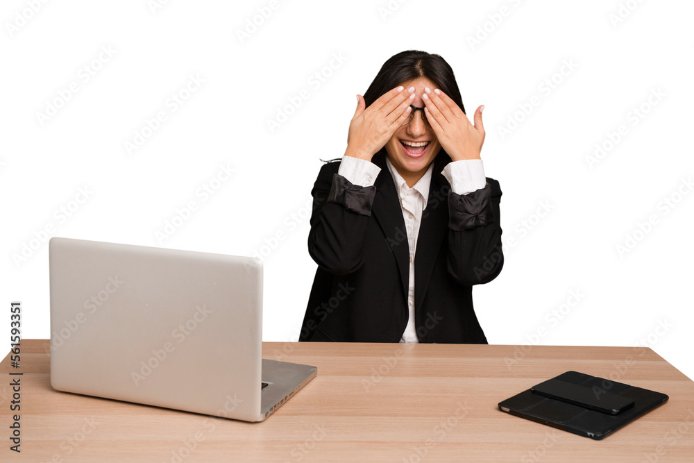 Young indian woman in a table with a laptop and tablet isolated covers eyes with hands, smiles broadly waiting for a surprise. Young indian woman in a table with a laptop and tablet isolated covers eyes with hands, smiles broadly waiting for a surprise.