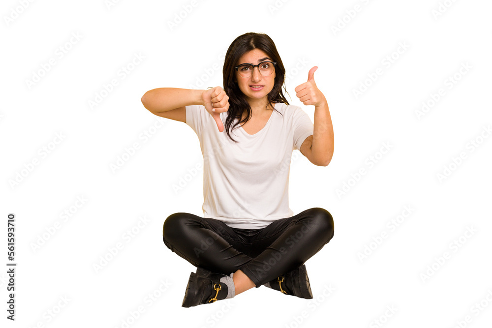 Young indian woman sitting on the floor cut out isolated showing thumbs up and thumbs down, difficult choose concept Young indian woman sitting on the floor cut out isolated showing thumbs up and thumbs down, difficult choose concept