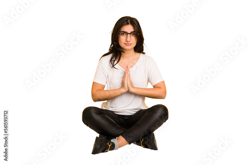 Young indian woman sitting on the floor cut out isolated praying, showing devotion, religious person looking for divine inspiration.