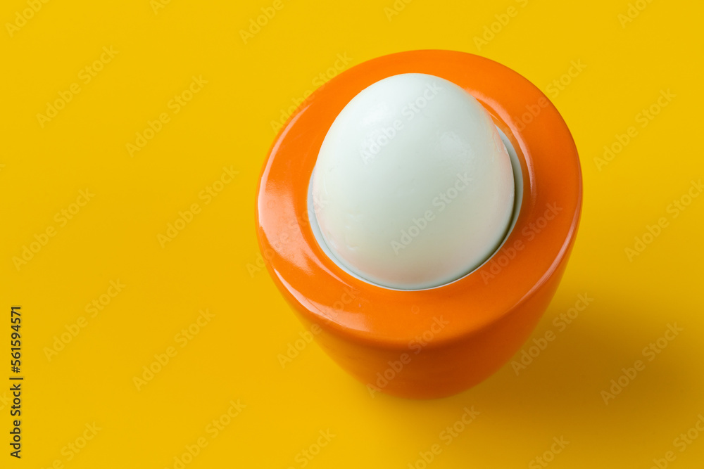 boiled egg in an orange stand on a yellow background, original design, the concept of reviving, valuable nutrients, protein and vitamins