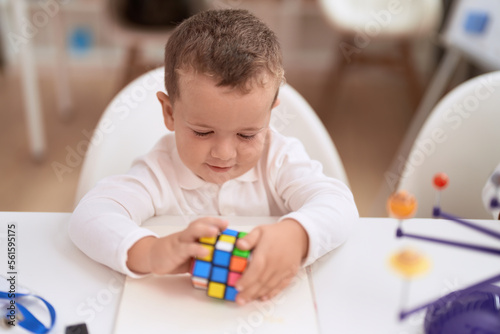 фотографія Adorable toddler playing with rubik cube sitting on table at kindergarten