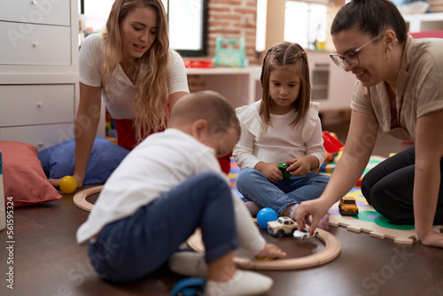 Teachers with boy and girl playing with cars toy sitting on floor at kindergarten