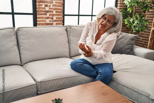 Middle age woman sitting on sofa suffering for wrist pain at home