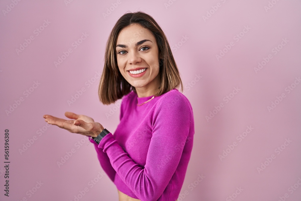 Hispanic woman standing over pink background pointing aside with hands open palms showing copy space, presenting advertisement smiling excited happy Hispanic woman standing over pink background pointing aside with hands open palms showing copy space, presenting advertisement smiling excited happy