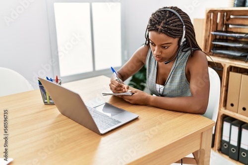 Young african american woman call center agent writing on notebook at office