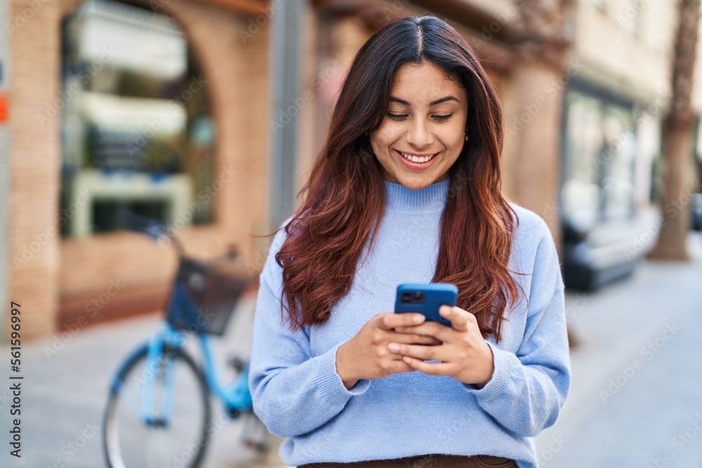 Young hispanic woman smiling confident using smartphone at street