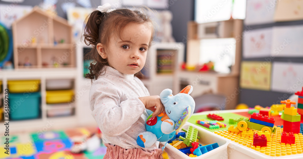 Fototapeta premium Adorable hispanic toddler holding elephant toy standing at kindergarten