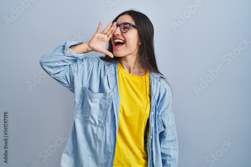 Konstfotografi Young hispanic woman standing over blue background shouting and screaming loud to side with hand on mouth