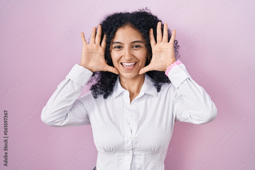Hispanic woman with curly hair standing over pink background smiling cheerful playing peek a boo with hands showing face. surprised and exited Hispanic woman with curly hair standing over pink background smiling cheerful playing peek a boo with hands showing face. surprised and exited