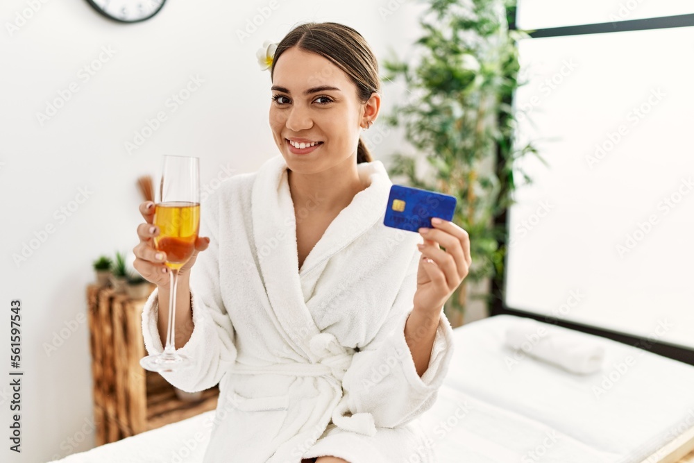Young hispanic woman holding credit card drinking champagne at beauty center. Young hispanic woman holding credit card drinking champagne at beauty center.