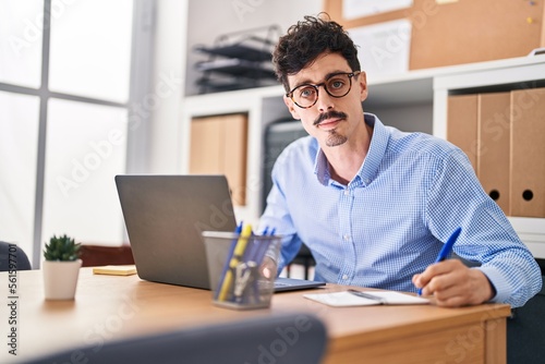 Young caucasian man business worker using laptop writing on notebook at office