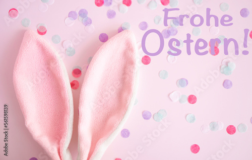 Easter greeting card .Pink bunny ears on pink pastel background wint confetti with text Frohe .Ostern . Easter minimal concept. flat lay