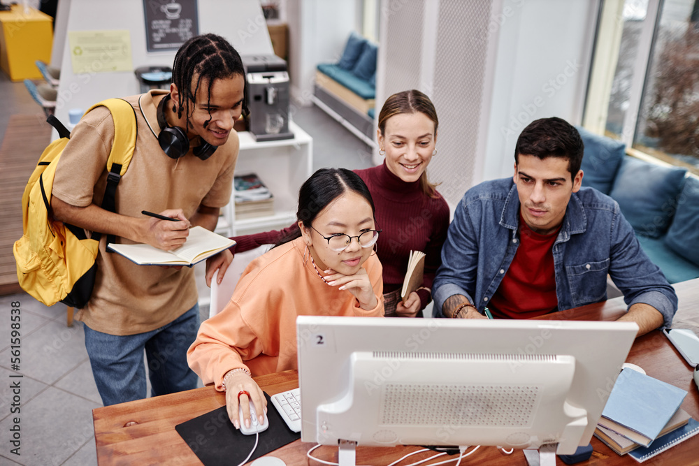 © Seventyfour - Diverse group of college students using computer together in library