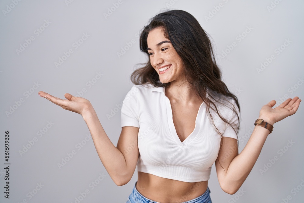 Young teenager girl standing over white background smiling showing both hands open palms, presenting and advertising comparison and balance Young teenager girl standing over white background smiling showing both hands open palms, presenting and advertising comparison and balance
