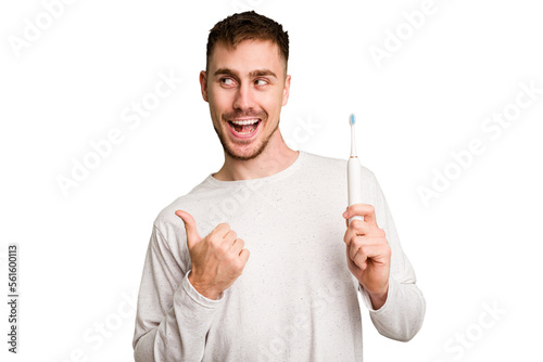 Young caucasian man holding an electric toothbrush isolated cut out points with thumb finger away, laughing and carefree.