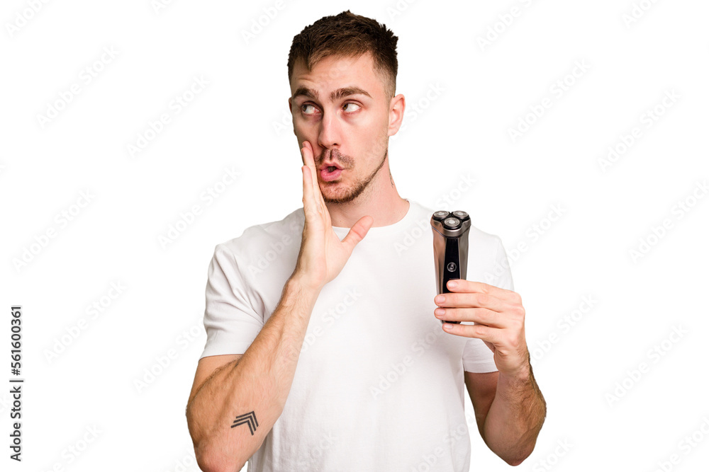 Young man holding a shaving machine cut out isolated is saying a secret hot braking news and looking aside