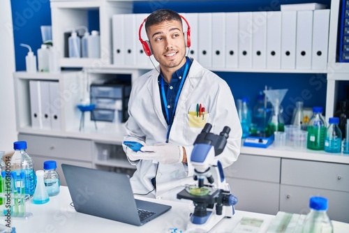 Young hispanic man scientist using laptop and smartphone at laboratory