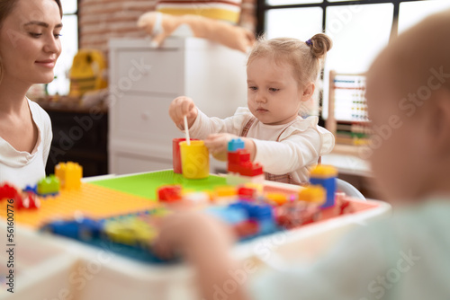 Teacher with boy and girl playing with construction blocks sitting on table at kindergarten