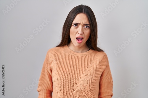Young brunette woman standing over white background in shock face, looking skeptical and sarcastic, surprised with open mouth © Krakenimages.com