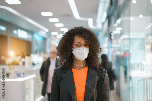COVID-19 Pandemic Coronavirus. Portrait young African american girl wearing face mask ffp2 walk in the mall