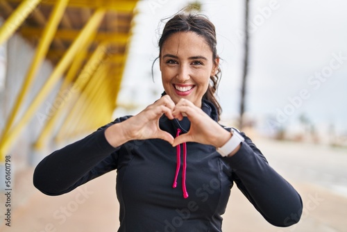 Young hispanic woman wearing sportswear doing heart symbol with hands at street