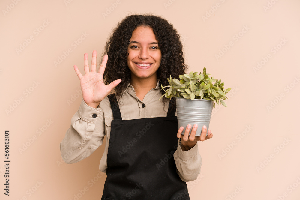 Young african american gardener woman holding a plant isolated smiling cheerful showing number five with fingers. Young african american gardener woman holding a plant isolated smiling cheerful showing number five with fingers.