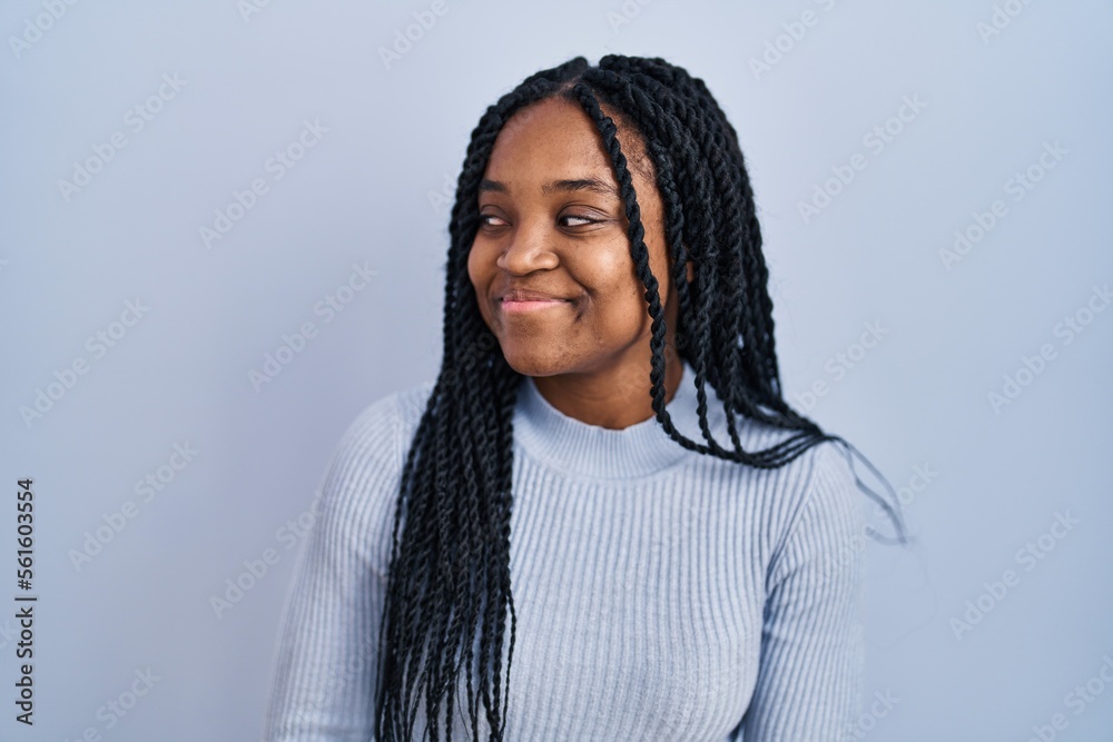 African american woman standing over blue background smiling looking to the side and staring away thinking. African american woman standing over blue background smiling looking to the side and staring away thinking.