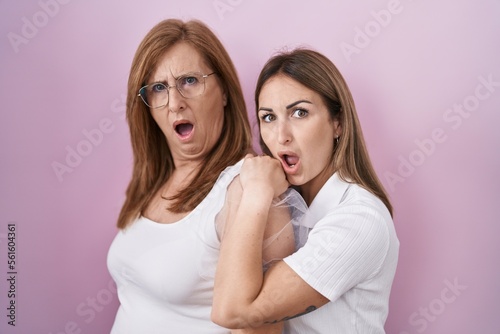 Hispanic mother and daughter wearing casual white t shirt in shock face, looking skeptical and sarcastic, surprised with open mouth