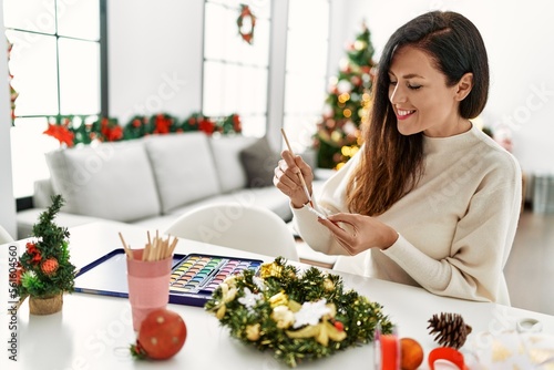 Middle age hispanic woman make christmas decor sitting on the table at home