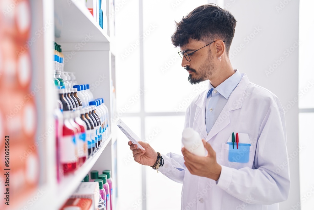 Young hispanic man pharmacist holding pills bottle reading preascription at pharmacy