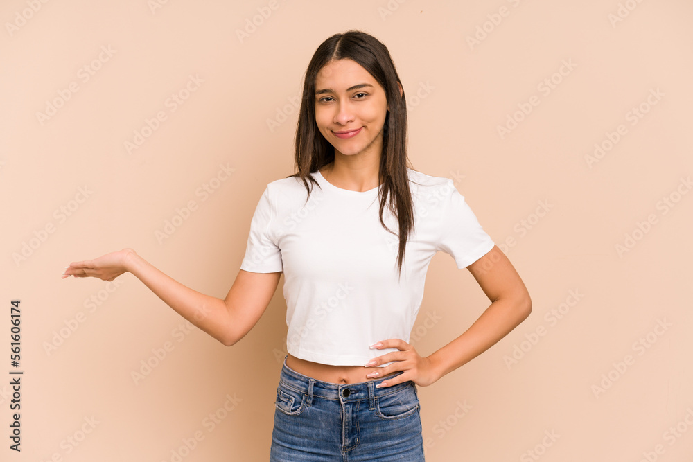 Φωτογραφία Young colombian woman isolated on beige background showing a copy space on a palm and holding another hand on waist