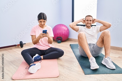 Man and woman couple smiling confident training abs exercise using smartphone at sport center