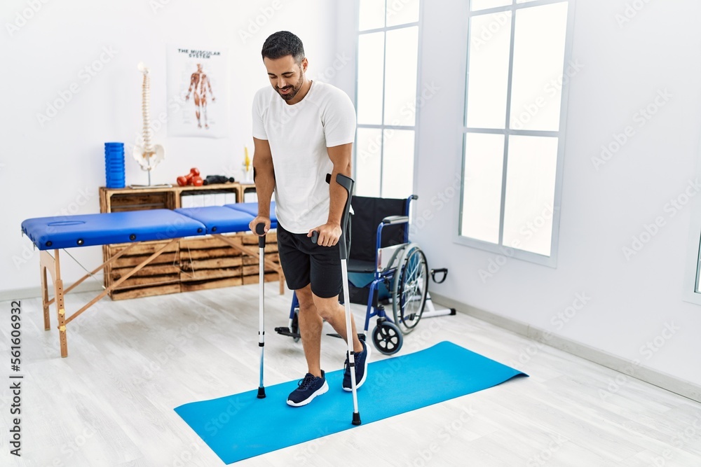 Fototapeta premium Young hispanic man patient having rehab session walking using crutches at clinic