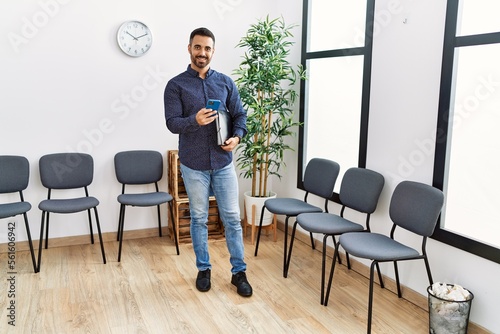 Young hispanic man using smartphone standing at waiting room