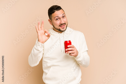 Young latin man holding a cola refreshment isolated cheerful and confident showing ok gesture.