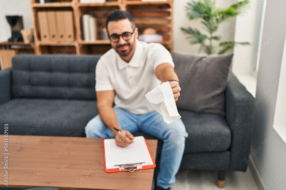 Young hispanic man psychologist writing on clipboard holding napkin at psychology center Young hispanic man psychologist writing on clipboard holding napkin at psychology center
