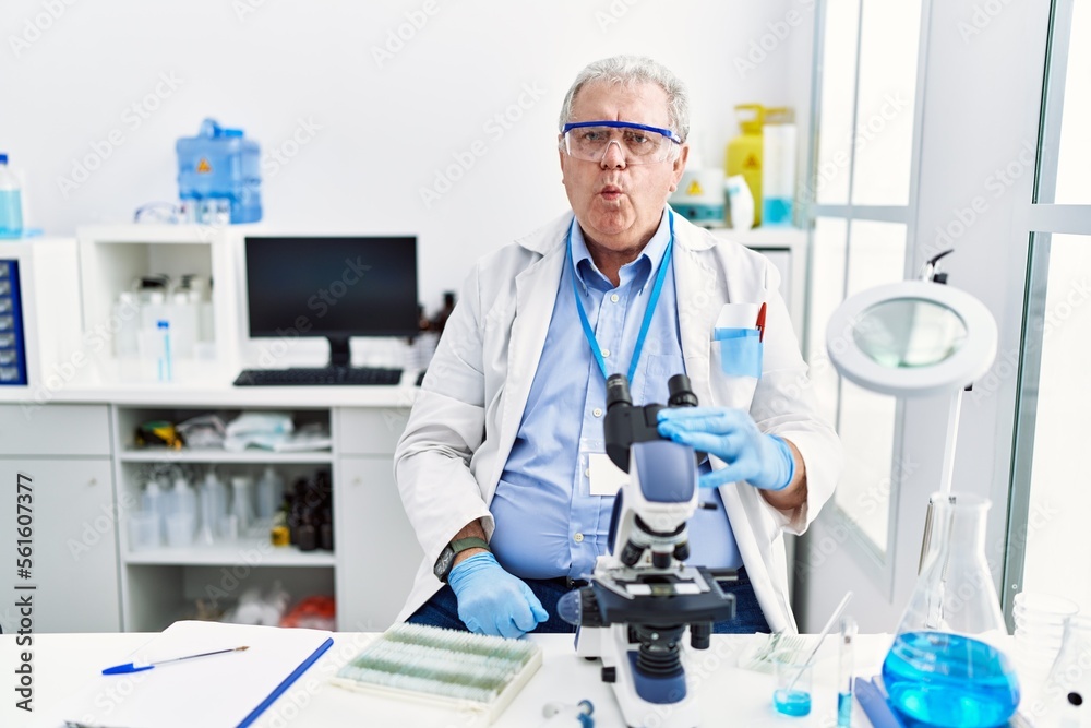 Senior caucasian man working at scientist laboratory making fish face with lips, crazy and comical gesture. funny expression. Senior caucasian man working at scientist laboratory making fish face with lips, crazy and comical gesture. funny expression.