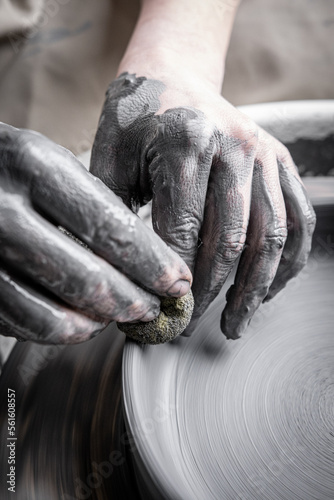 Women working at pottery wheel, creating dishes. The dirty hands of the potter in the clay and on the wheel. Creation.
